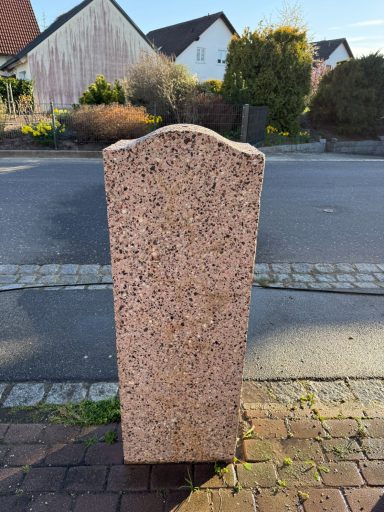 Ein rechteckiger, grauer Stein mit einer leicht gewölbten Oberkante auf einem Bürgersteig.
