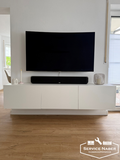 Moderner Wohnbereich mit einem großen Fernseher über einem weißen TV-Unterschrank. Möbelaufbau durch Service Naber in Amberg