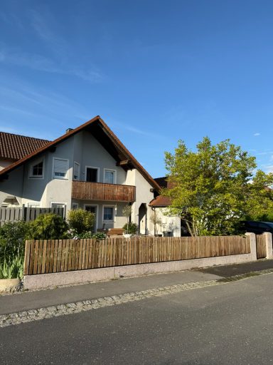 Ein modernes Haus mit Dachgaube, Garten und Holzzaun an einer ruhigen Straße.