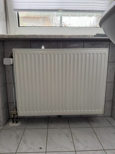 Heizkörper in einem Badezimmer mit Fliesenboden und Fenstern.